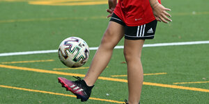 Ein Mädchen steht auf einem Fußballplatz und kickt den Ball in die Luft.