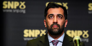 Humza Yousaf sitzt vor einem Mikrofon und schaut nach oben