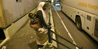 Eine Frau steht mit einem Kind auf dem Rücken vor einem Reisebus