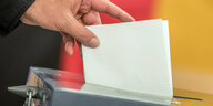 Eine Hand steckt einen Zettel in eine Wahlurne