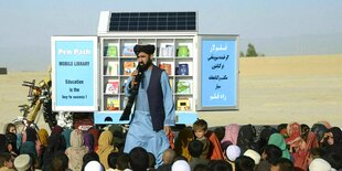 Matiullah Wesa steht vor einer fahrbaren Bibliothek und spricht zu Kindern, die vor ihm auf dem Boden sitzen