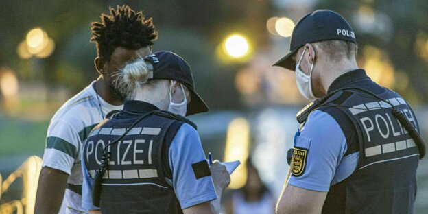 Zwei Polizistenstehen mit einem jungen Schwarzen auf der Straße und notieren sich etwas