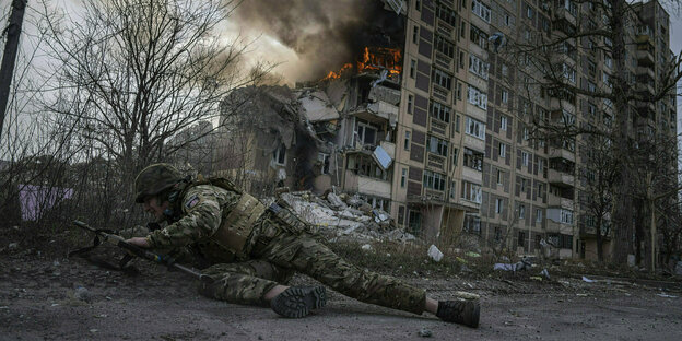 A soldier takes cover in front of a burning house