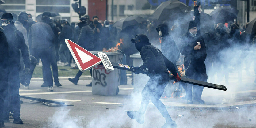 Ein schwarz gekleideter Mann hält ein Straßenschild in der Hand