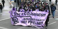Eine Demozug unterwegs auf der STraße- die Aktivisten tragen ein Lila Transparent mit der Aufschirft: Gas=CO²Ionalism - build Solidarity not Pipelines