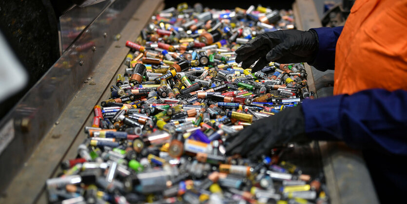 Sortierband mit vielen alten Batterien. Zwei Hände mit blauen Handschuhen sortieren sie.