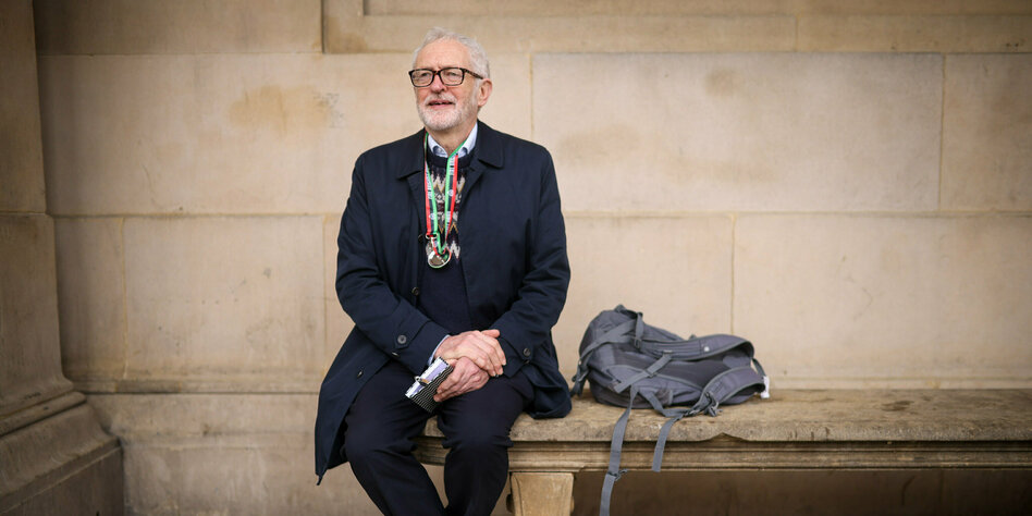 Corbyn sitzt auf einer Steinback im schwarzen Mantel