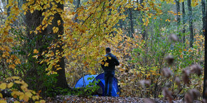 Mann steht vor einem Zelt im Wald