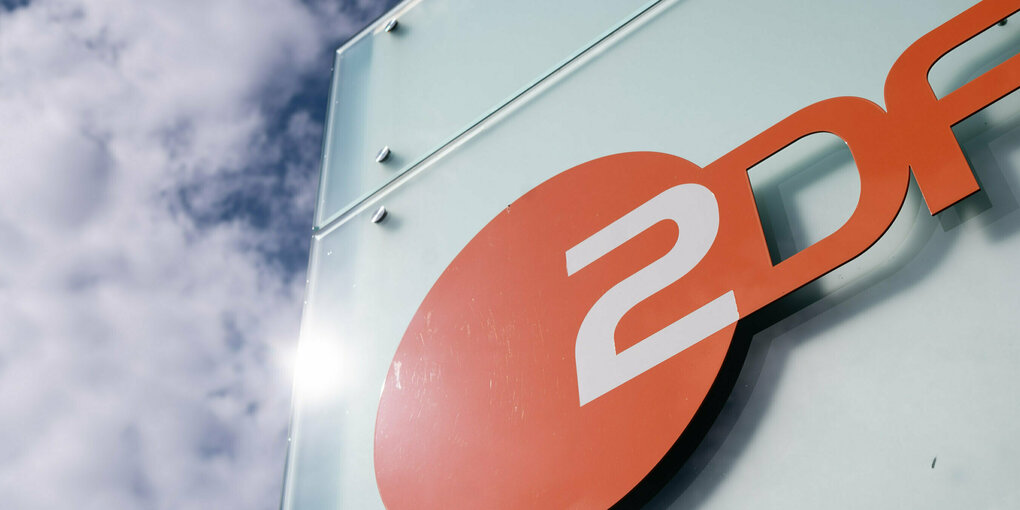 Eine weiße, glänzende Häuserwand, darauf Schräg das Logo und der Schriftzug vom ZDF. Dahinter blauer Hillem mit Wolken. Die Sonne blitzt an der Hauswand ab.