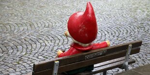 Eine Skulptur des Sandmännchens sitzt auf einer Holzbank