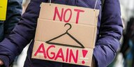 Eine Frau trägt ein Plakat um den Hals mit der Aufschrift: "Not Again" und einem gemalten Kleiderbügel