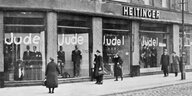 Menschen stehen vor einem Geschäft, auf den Schaufensterscheiben steht fünf mal groß das Wort Jude