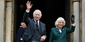 Prinz Charles und seine Frau Camilla stehen winkend vor einem Hauseingang.