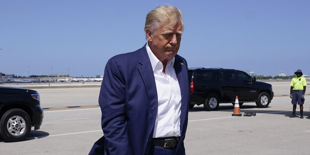 Trump mit gesenktem Kopf auf einem Flugplatz, seitlich fotografiert