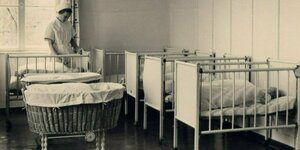 Krankenschwester steht inmitten von Gitterbetten mit Säuglingen