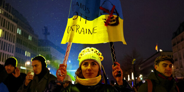 Eine Frau hält bei einer Demo ein blau glebes Plakat
