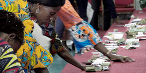 Menschen in afrikanischen Gewändern beugen sich über eine Treppe, auf der Geldbündel liegen