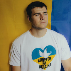 Der Athlet Wladyslaw Heraskewytsch hat kurze dunkelblonde Haare, trägt ein weißes T-Shirt mit der Aufschrift Athletes for Ukraine