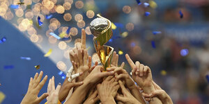 Viele Hände halten gemeinsam den WM-Pokal