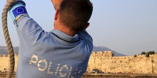 Ein Mann in Polizei-T-Shirt ist von hinten zu sehen.