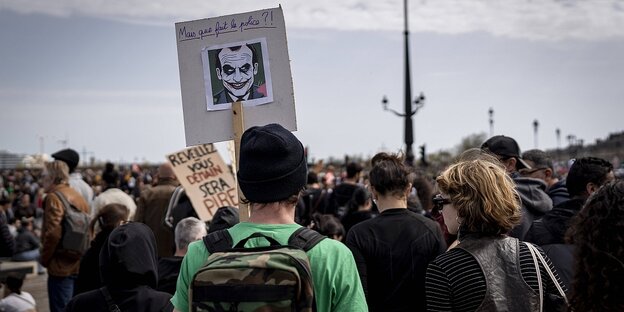 Menschen protestieren, einer trägt ein Schild, auf dem Emmanuel Macron als Batman zu sehen ist