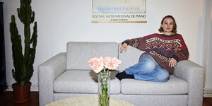 Inger Nordvik sitzt auf dem hellen Sofa daneben ein sehr großer Kaktus, auf dem Tisch steht ein Strauß Blumen