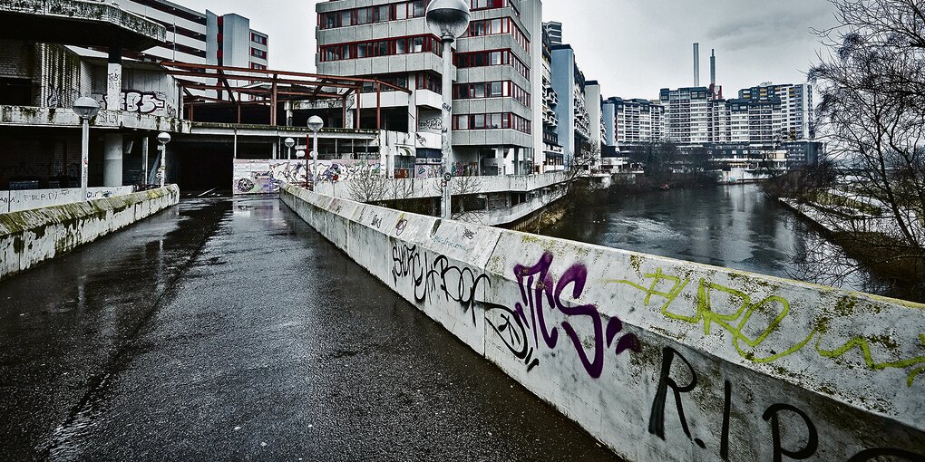 Eine vollgekritzelte Beton-Brücke führt zu hohen Häusern aus dreckig-schwarzem Beton.