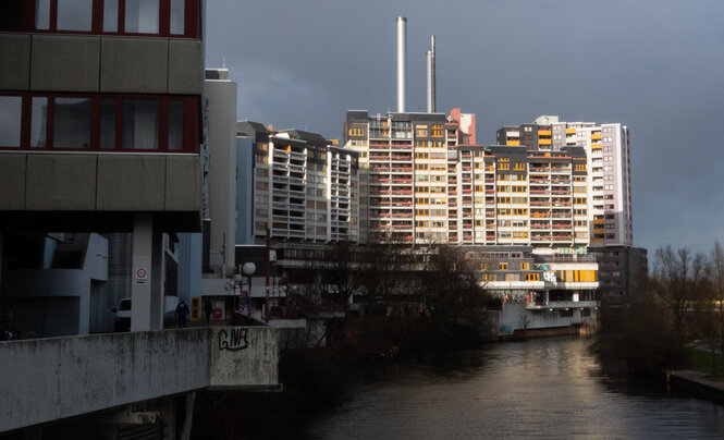 Ein Hochhaus am Fluß, davor ein Gebäude aus Sichtbeton.