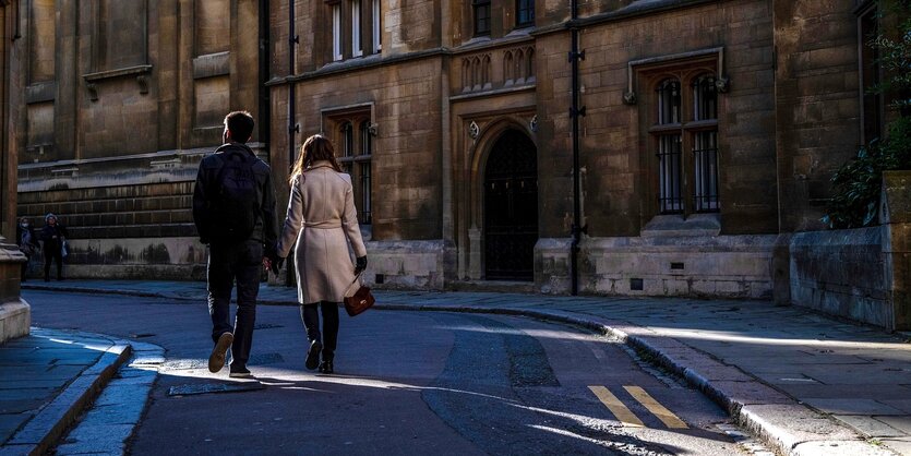 Ein Paar geht an Gebäuden der Universität Cambridge in England vorbei