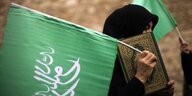 Eine verschleierte Frau trägt eine grüne Fahne und den Koran