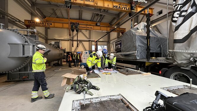 Drei Männer mit Warnwesten stehen im Lagerraum und besprechen die Installation der Flusswärmepumpe