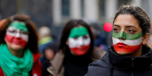 Drei Frauen haben ihre Gesichter in den Landesfarben des Iran geschminkt
