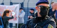 Ein Polizist mit Mundschutzmaske, im Hintergrund ein Transparent und viele Menschen