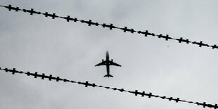 Flugzeug am Himmel, davor Stacheldraht