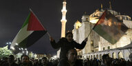 Demonstrierende, ein Vater hält seine Tochter auf den Schultern, sie hält in beiden Händen Flaggen der palästinensichen Autonomiegebiete, im Hintergrund eine nächtlich erleuchtete Moschee