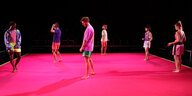 Tänzer und Tänzerinnen stehen auf einer Bühne mit rotem Boden