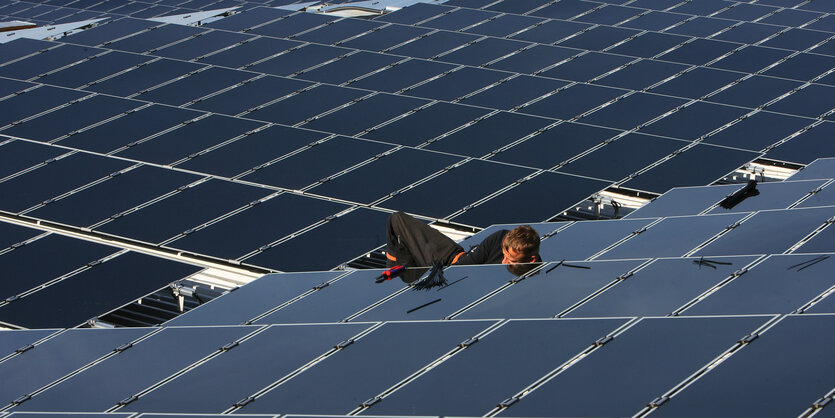 Ein Mann arbeitet hinter einem schwarzen Solarmodul in einem Feld von Solarmodulen