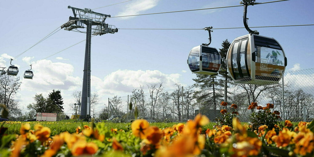 Kabinen der Seilbahn fahren auf dem Gelände der Bundesgartenschau hinter einem Blumenbeet