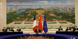 Xin Jinping sitzt vor großem Peking-Bild und den Flaggen von Frankreich, China und der EU