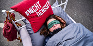 Eine Frau liegt in einem Bett mit einem Kopfkissen, das die Aufschrift "Nicht genesen" trägt
