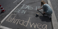 Mensch schreibt mit Kreide auf Straße "Das ist dein Fahrradweg"