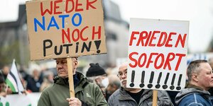 Zwei Männer halten auf dem Berliner Ostermarsch Plakate mit folgender Aufschrift hoch: „Weder Nato noch Putin" und „Frieden sofort“
