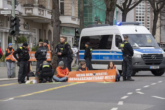 Aktivisten sitzen auf der Straße, dahinter ein Polizeiwagen