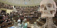 Hörsaal mit Studierenden im Vordergrund ein menschliches Skelett