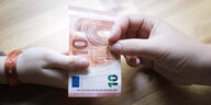 Eine Hand reicht einer anderen Hand einen 10-Euro-Schein
