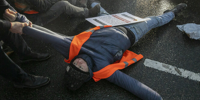 Eine Person versucht einen Aktivisten der Letzten Generation von der Straße zu zerren