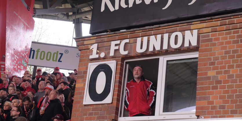 Götz Geserick tauscht bei jedem Tor die Tafel im Stadion An der Alten Försterei aus - analog, also per Hand, man kann den Mann in einem offenen Fenster sehen, neben ihm eine große Null - die Ziffer hängt an einem Haken