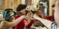 Menschen in eienm Restaurant erheben die Wein- Gläser und stoßen gemeinsam an