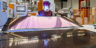 Eine Frau hält in einer Fabrik eine Solarfolie hoch
