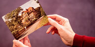 Die Hände einer Frau halten ein altes Foto, auf dem die ehemalige Kinderheilanstalt "Waldhaus" in Bad Salzdetfurth in Niedersachsen zu sehen ist.